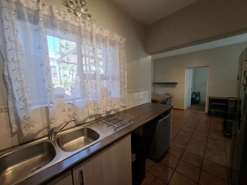 A functional kitchen area featuring a double bowl stainless steel sink, laminate countertops, and tiled flooring, leading into an adjacent living space.