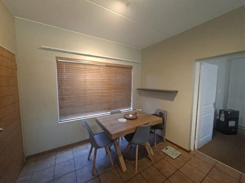 A functional dining area featuring tiled flooring, a floating wall shelf, and venetian blinds, providing a neutral space for meals.