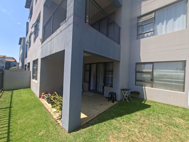Rear view of the apartment building featuring a ground floor covered patio, upper-level balcony with metal railing, and well-maintained lawn area.