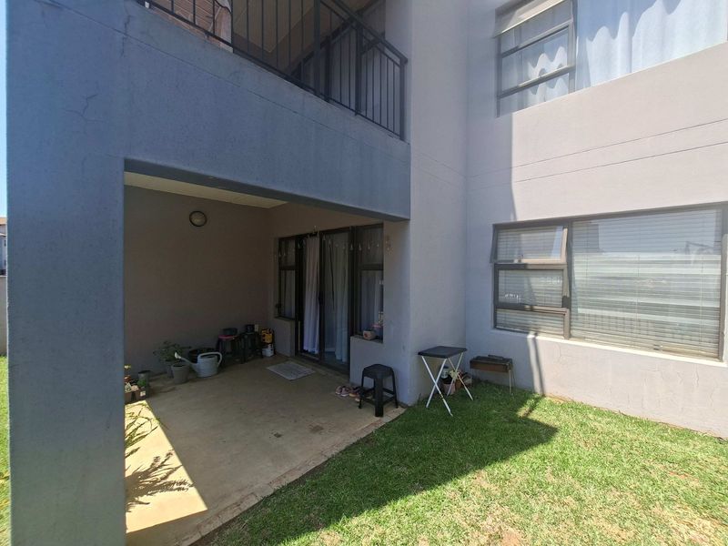 A covered ground-floor patio area featuring concrete flooring, sliding glass door access, and a small adjacent lawn space.