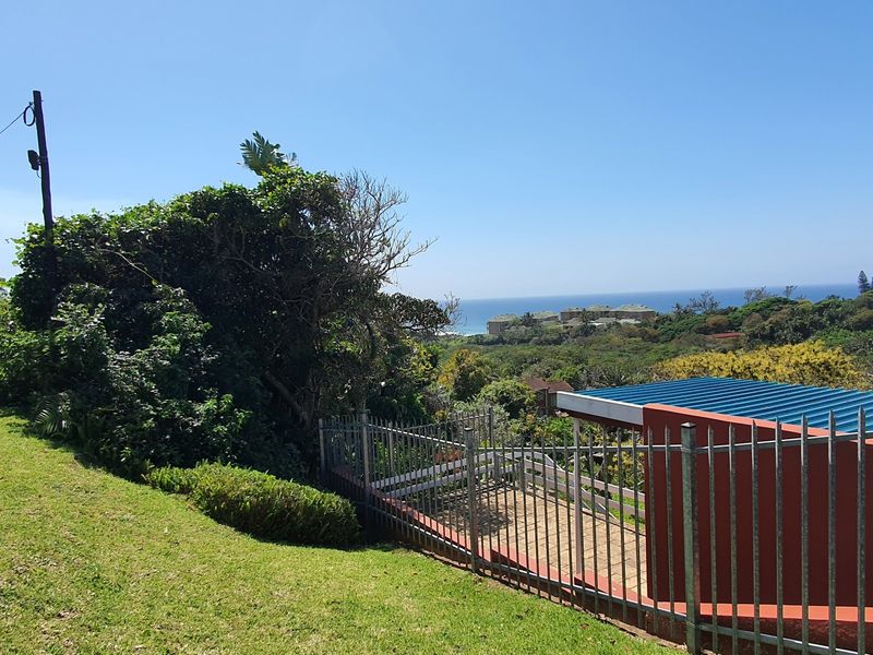 A scenic view overlooking coastal vegetation and the ocean, featuring a paved driveway and metal perimeter fencing on the property.