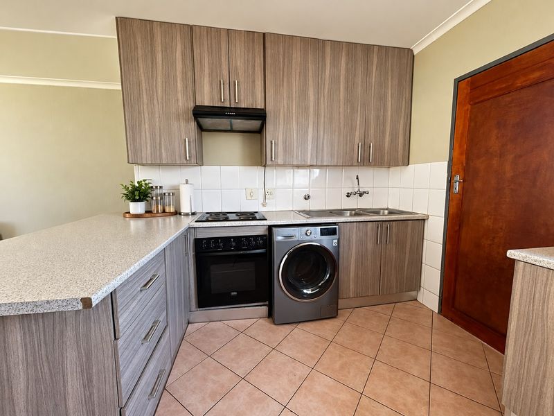 A functional kitchen featuring wood-grain cabinetry, laminate countertops, a built-in oven with hob, and tiled flooring with integrated laundry appliance space.