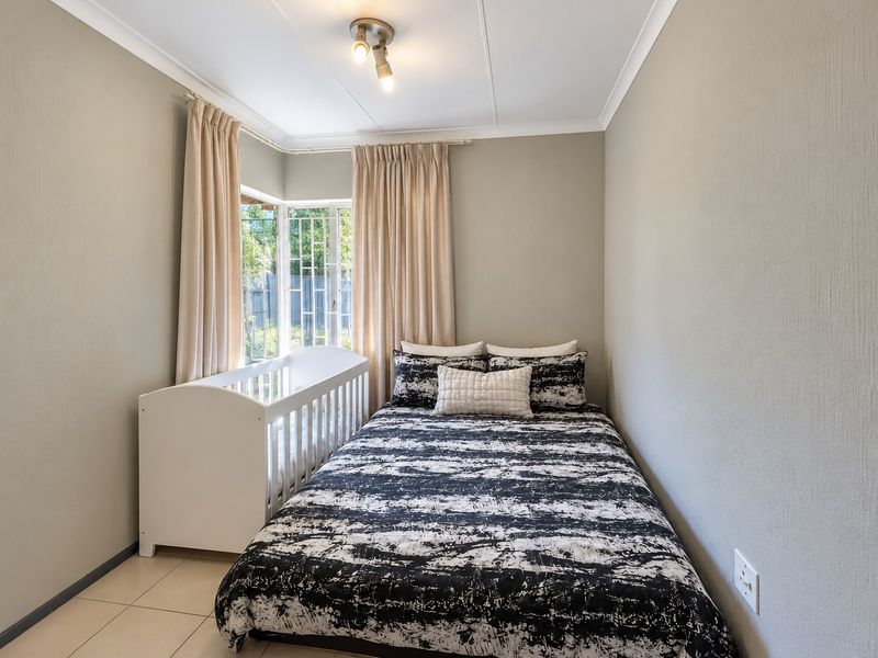 A compact bedroom featuring tiled flooring, a corner window with security bars, and neutral wall finishes.
