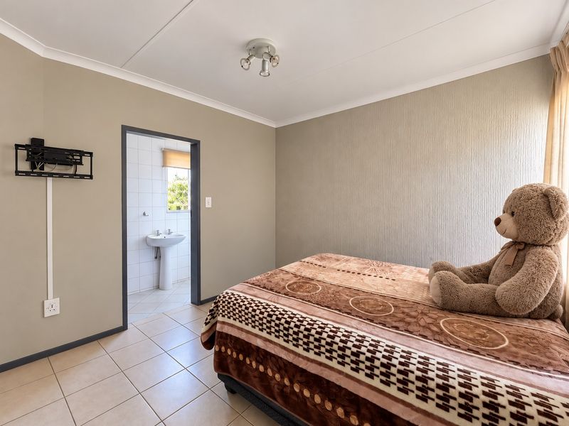 A bedroom featuring tiled flooring, textured accent wall, and direct access to an en-suite bathroom with a pedestal basin.