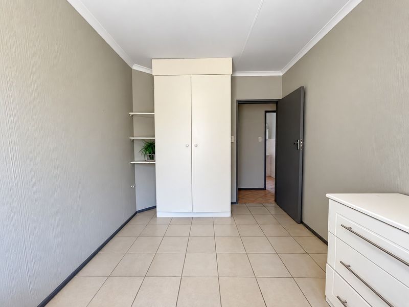 A clean, neutral bedroom featuring tiled flooring, a built-in wardrobe with integrated shelving, and access to an adjoining room.