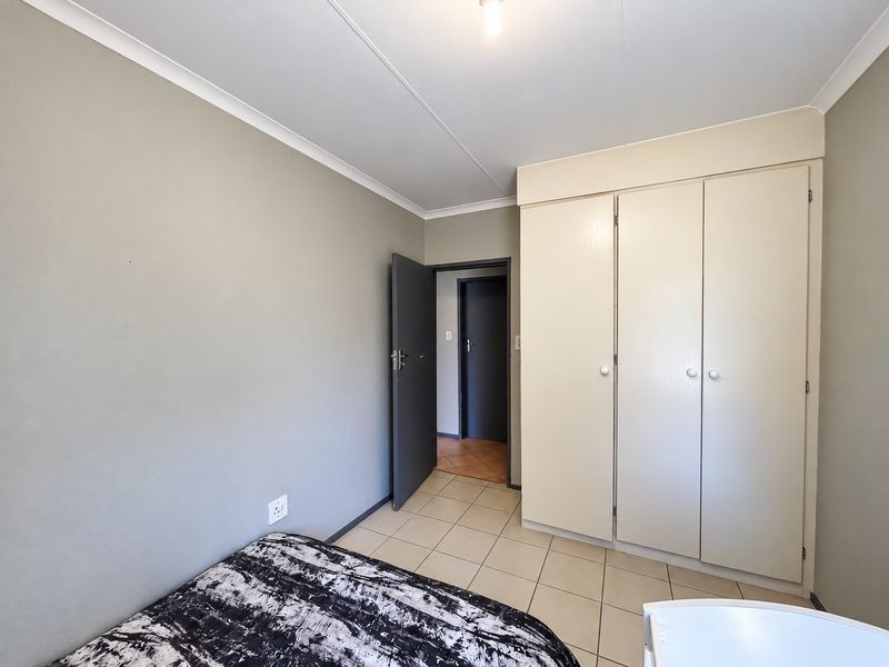 A bedroom featuring neutral wall tones, tiled flooring, and built-in cupboards, offering a functional and clean living space.