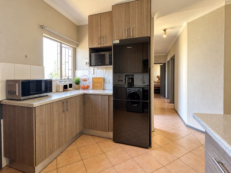 A functional kitchen featuring wood-look laminate cabinetry, durable countertops, and tiled flooring, with a convenient layout leading into the hallway.
