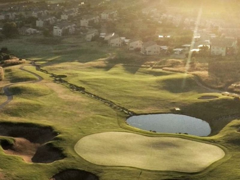 An aerial view of the surrounding golf course landscape, featuring manicured greens, sand bunkers, and water hazards at sunset.