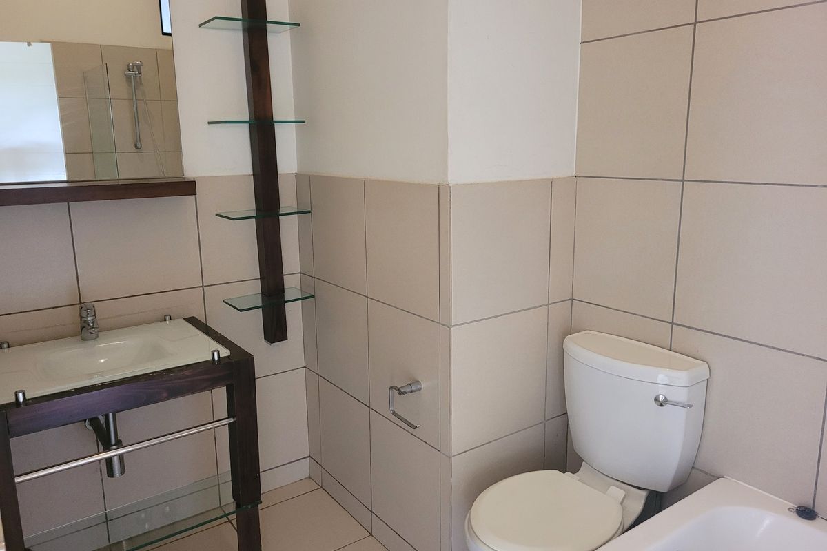 A clean, functional bathroom featuring a vanity basin, toilet, bathtub, and neutral wall tiling with integrated glass shelving.