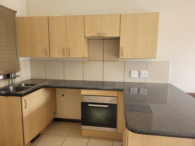 A functional kitchen featuring granite countertops, built-in oven, electric hob, and light wood-finish cabinetry with tiled backsplash and flooring.