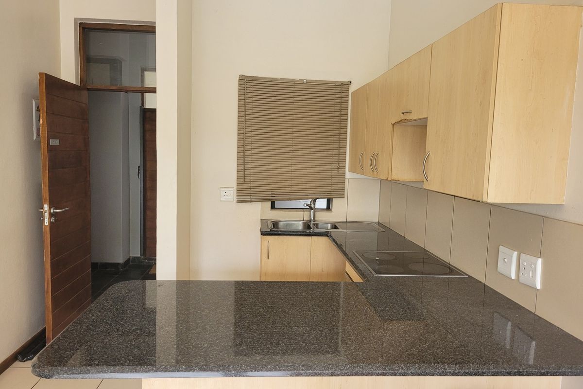A functional kitchen featuring granite countertops, built-in cabinetry, an electric hob, and a double sink, offering a clean and practical workspace.