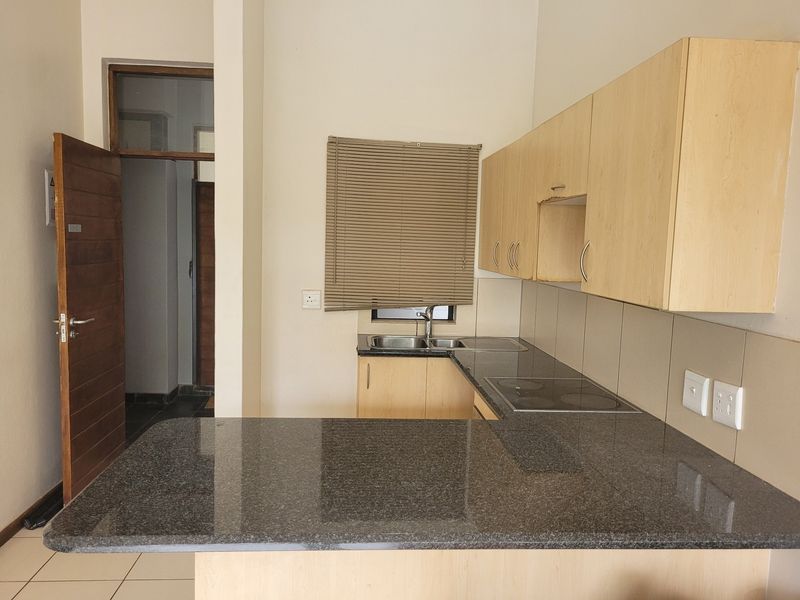 A functional kitchen featuring granite countertops, built-in cabinetry, an electric hob, and a double sink, offering a clean and practical workspace.