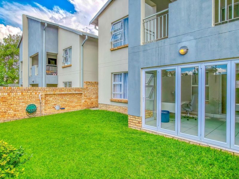 Rear view of the apartment featuring a private lawn, brick boundary wall, and modern bi-fold glass doors leading into the living area.