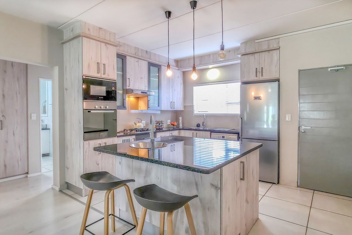 Modern kitchen featuring light wood-look cabinetry, a central island with a stone countertop, built-in appliances, and contemporary pendant lighting.