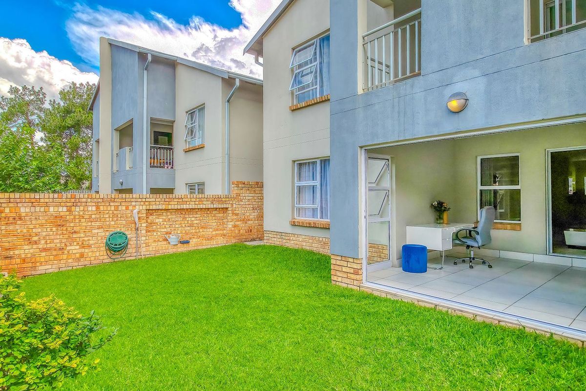 Rear view of the apartment featuring a private garden, brick boundary wall, and a tiled patio area accessible through folding glass doors.