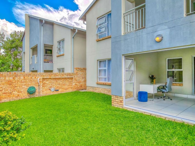 Rear view of the apartment featuring a private garden, brick boundary wall, and a tiled patio area accessible through folding glass doors.