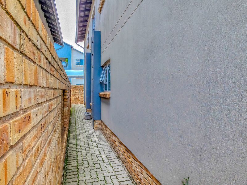 A narrow side passage featuring a paved walkway between a brick boundary wall and the plastered exterior wall of the apartment building.