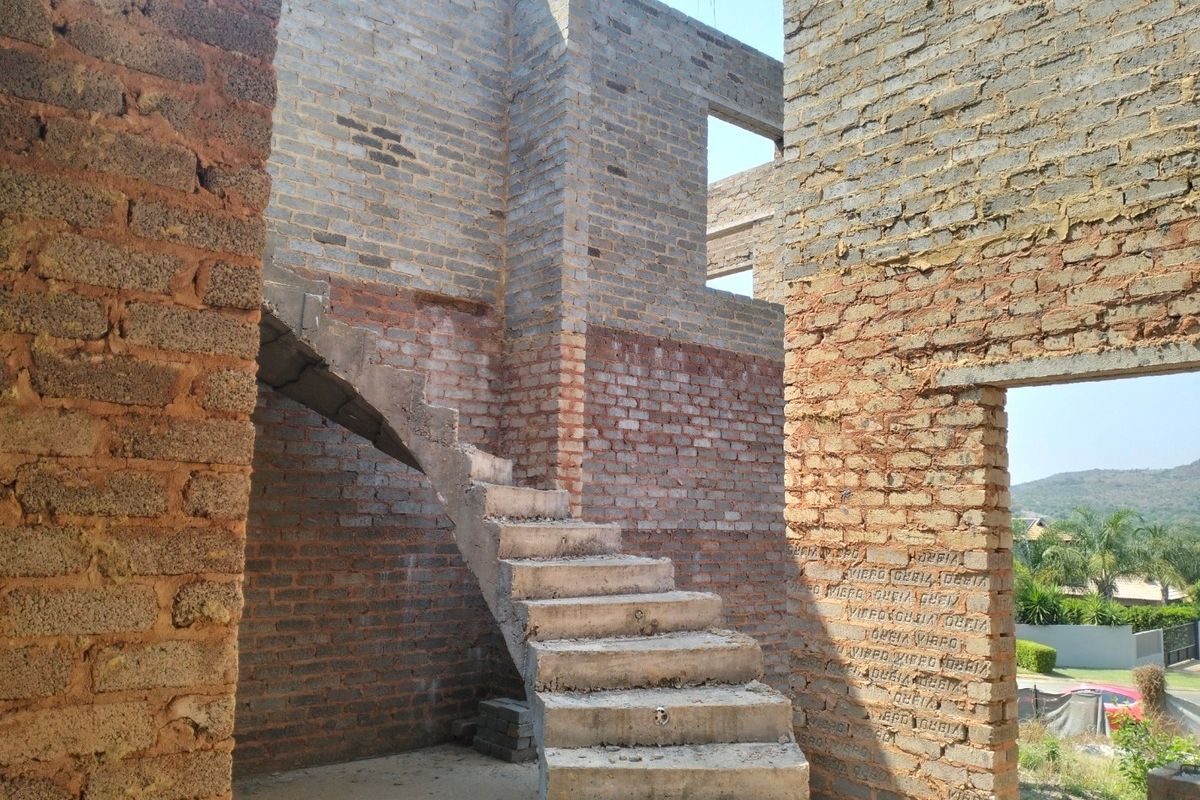An unfinished construction site featuring exposed brick walls and a concrete staircase, showing the structural shell of a property under development.