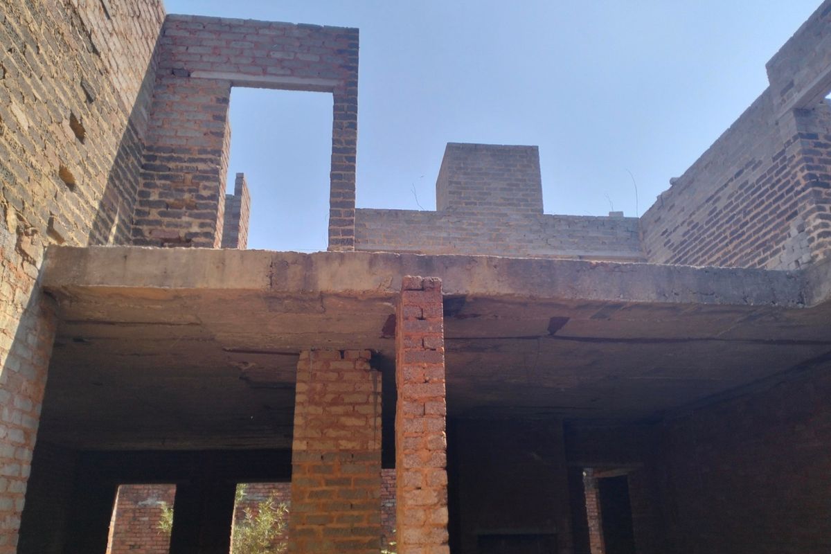 An unfinished residential structure showing exposed brick walls and concrete slab flooring, currently in the early stages of construction.