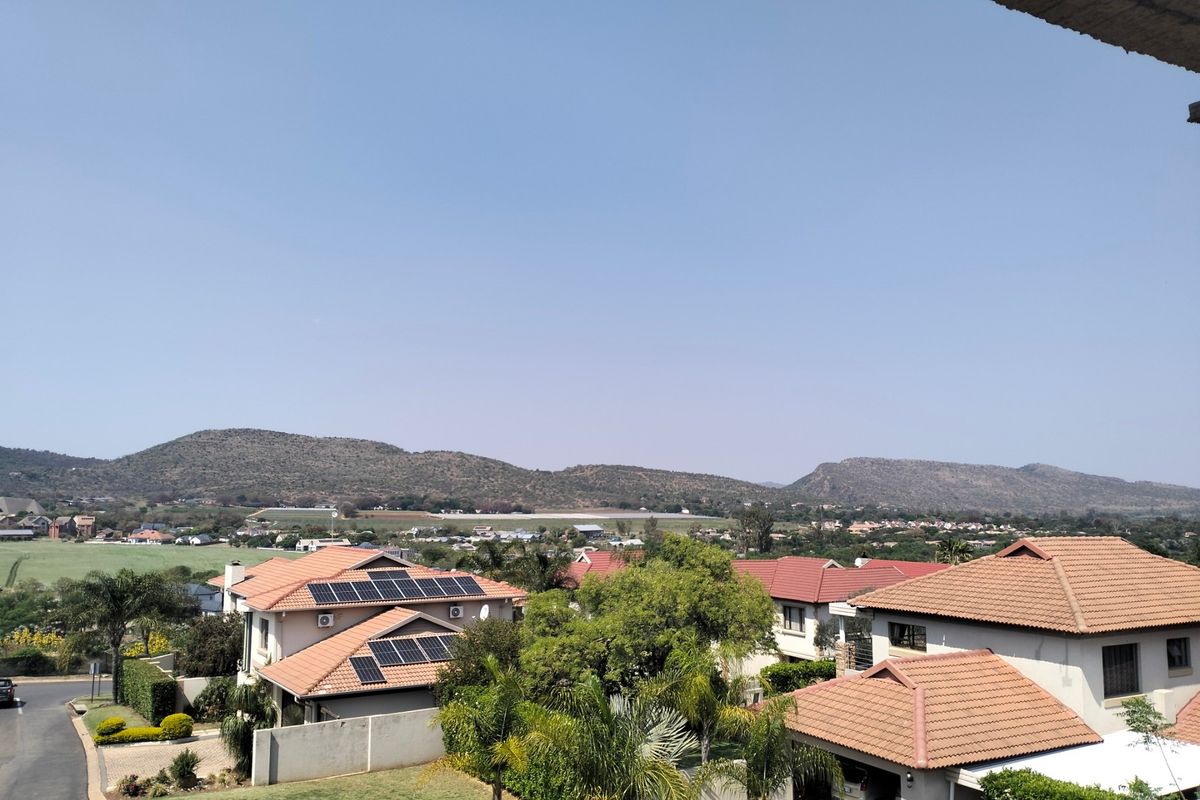 Elevated view overlooking a residential estate with mountain vistas, featuring homes with tiled roofs and solar panel installations.