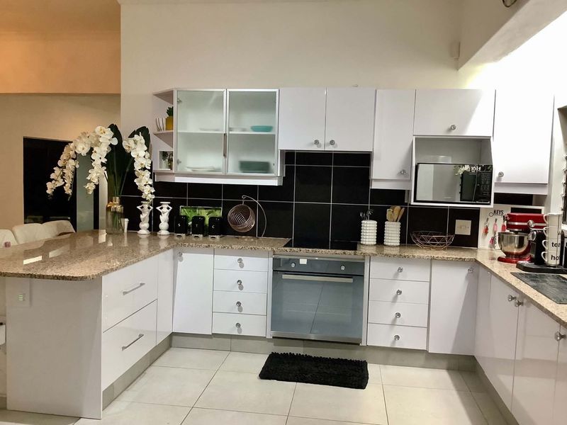 Modern kitchen featuring white cabinetry, granite countertops, a tiled backsplash, and integrated appliances including an oven and microwave.