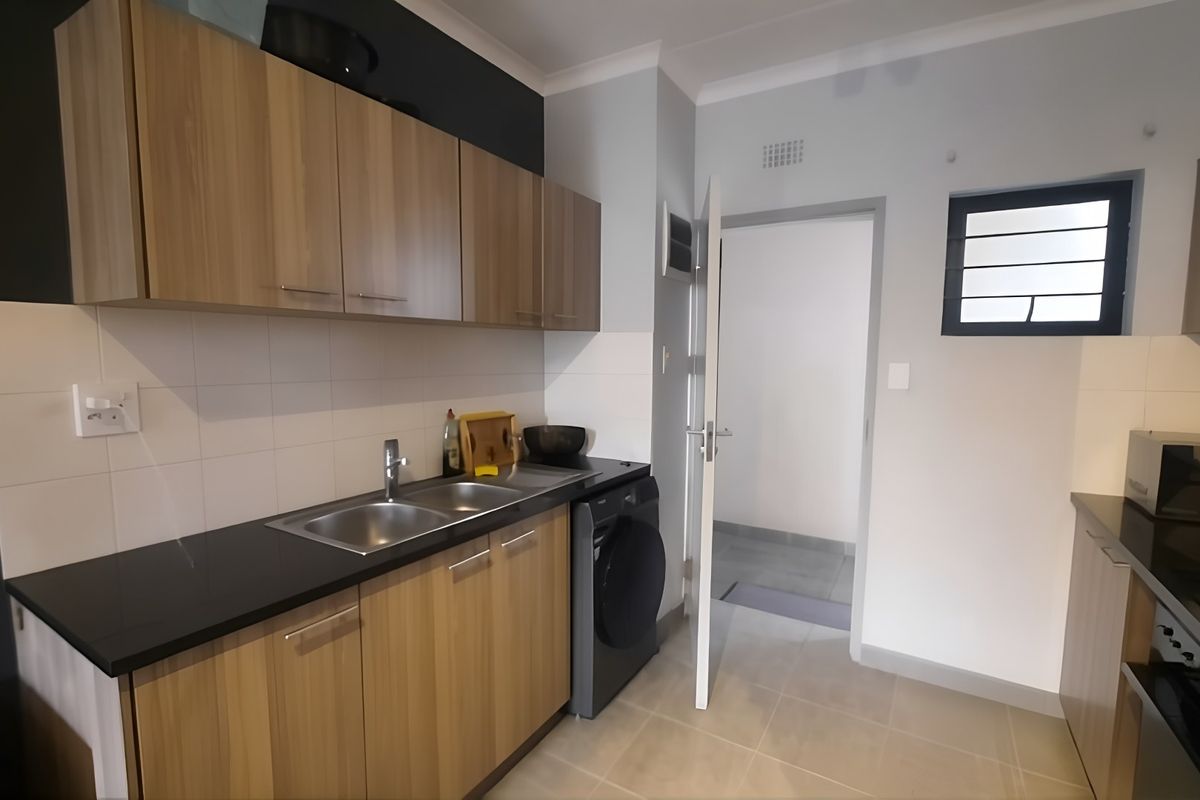 Modern kitchen featuring wood-look cabinetry, dark countertops, tiled splashbacks, and integrated appliances, offering a clean and functional workspace.