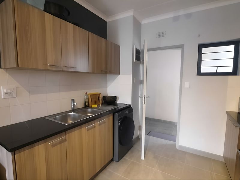 Modern kitchen featuring wood-look cabinetry, dark countertops, tiled splashbacks, and integrated appliances, offering a clean and functional workspace.