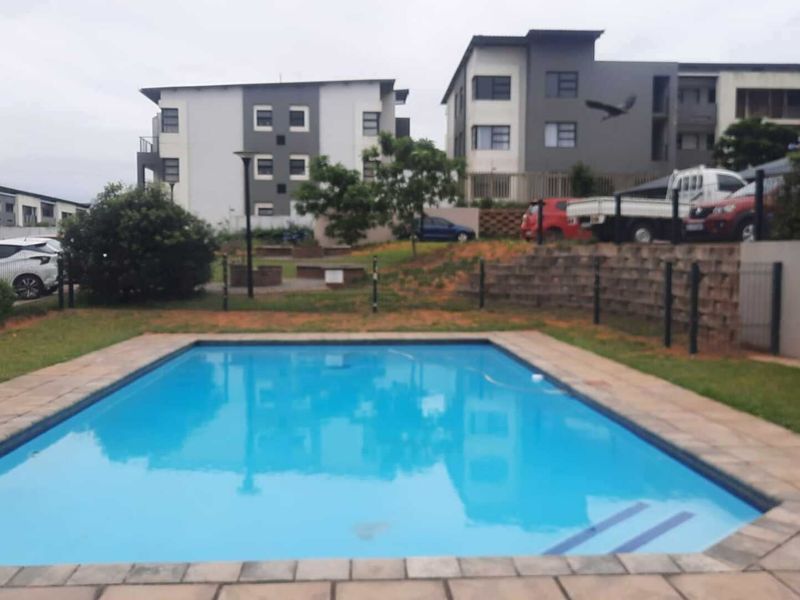 Communal swimming pool area featuring a paved surround, retaining wall, and perimeter fencing within an apartment complex setting.