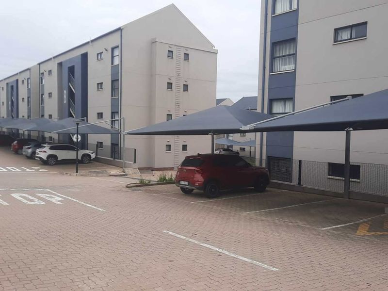 Exterior view of a modern apartment complex featuring paved parking areas with dedicated shade cloth carports for residents.