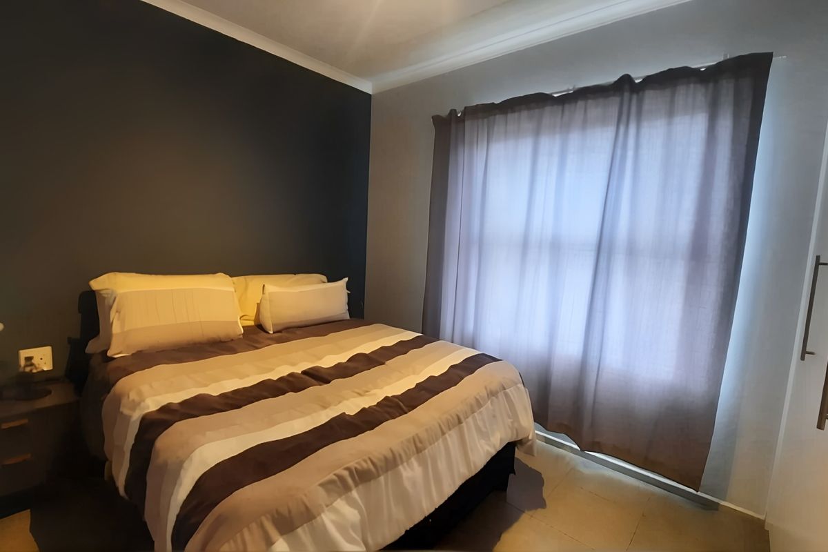A well-maintained bedroom featuring tiled flooring, a dark accent wall, and a built-in wardrobe with modern handles.