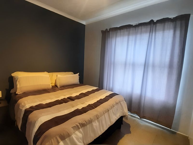 A well-maintained bedroom featuring tiled flooring, a dark accent wall, and a built-in wardrobe with modern handles.