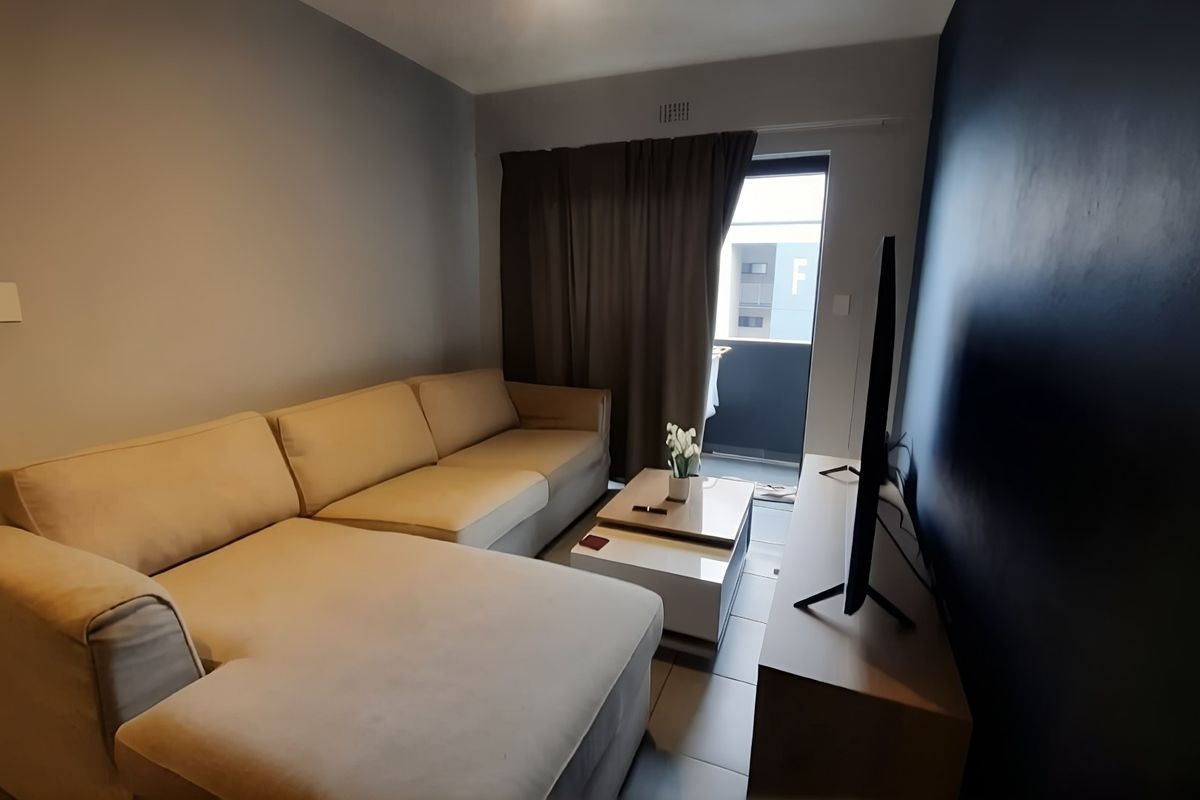 A modern living room featuring tiled flooring, a dark accent wall, and direct access to a private balcony through a sliding door.