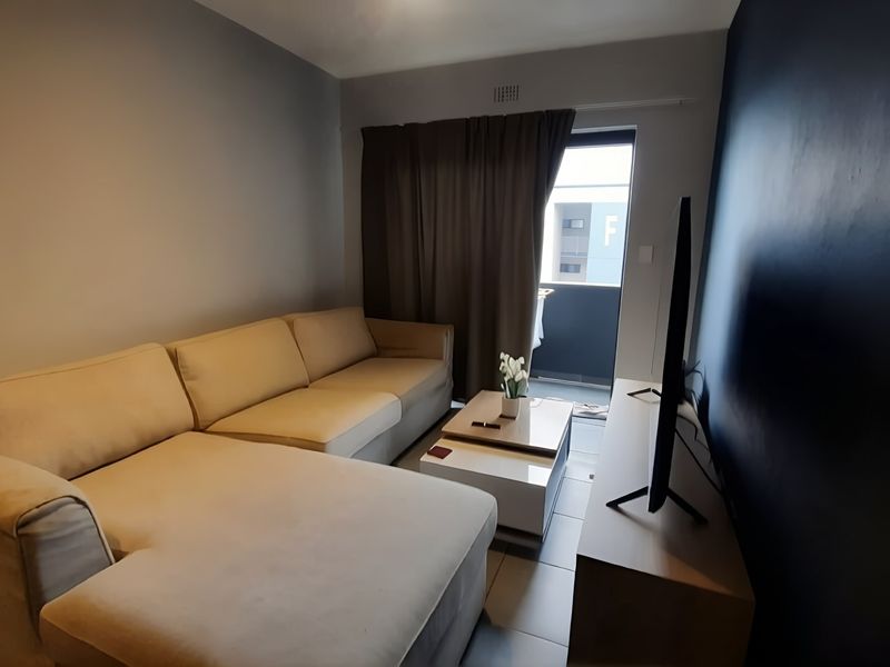 A modern living room featuring tiled flooring, a dark accent wall, and direct access to a private balcony through a sliding door.