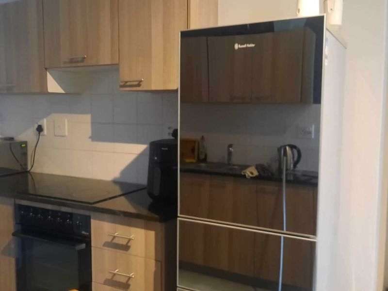 A functional kitchen featuring wood-look laminate cabinetry, dark granite countertops, a built-in oven with electric hob, and a tiled backsplash.