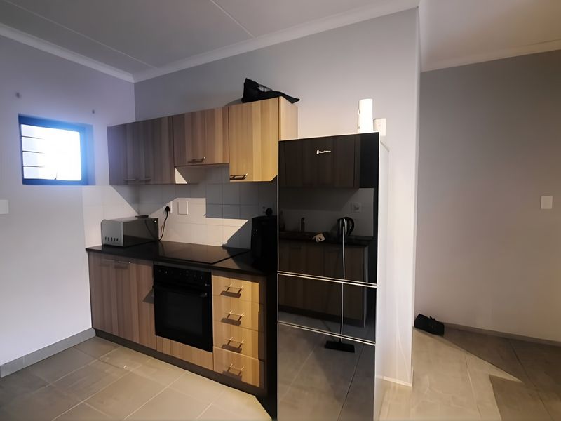 A functional kitchen featuring modern wood-finish cabinetry, integrated electric oven and hob, tiled backsplash, and neutral tiled flooring.