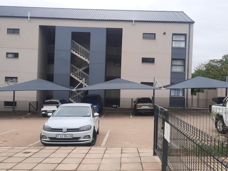 Exterior view of a multi-story apartment building featuring a paved parking area with shade cloth carports and an external metal staircase.