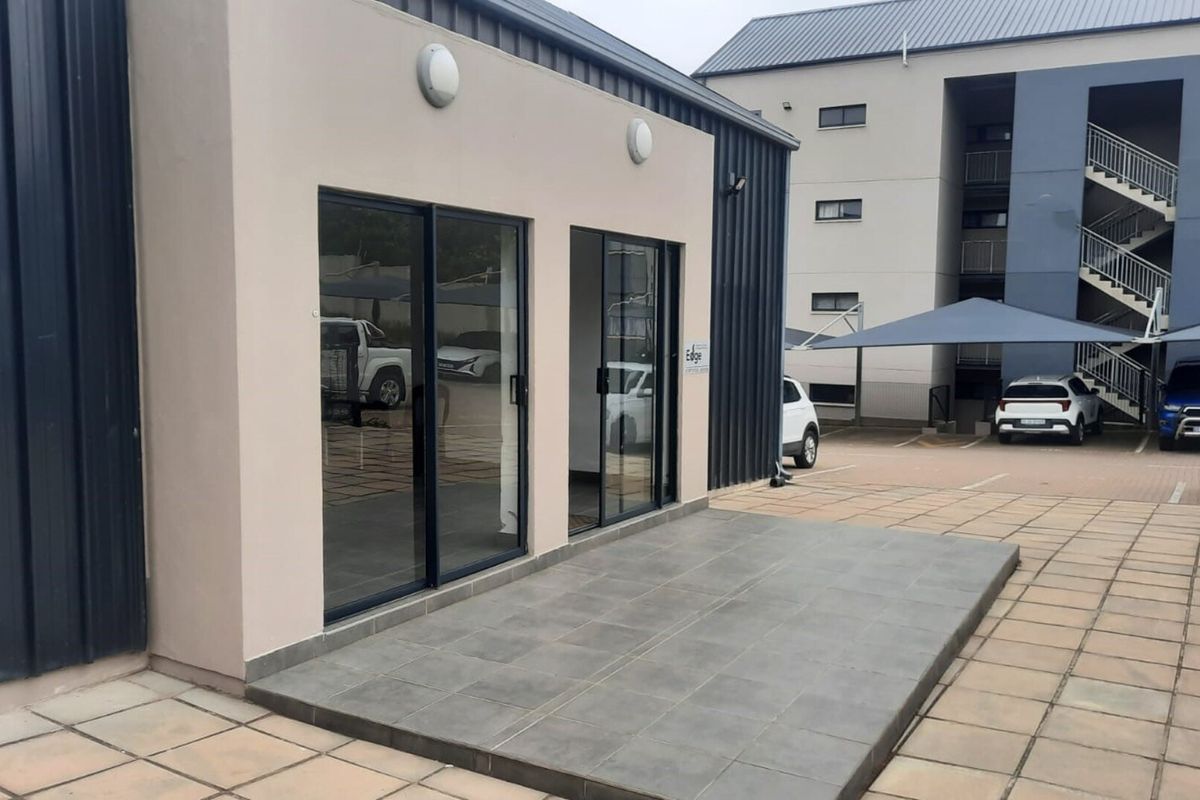 Exterior view of a modern apartment building featuring a paved patio area with sliding glass door access and adjacent parking facilities.