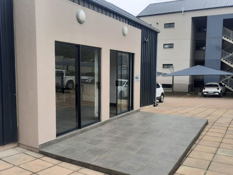 Exterior view of a modern apartment building featuring a paved patio area with sliding glass door access and adjacent parking facilities.