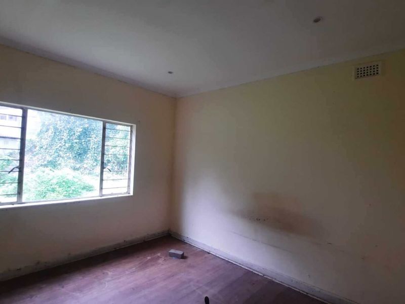 An empty bedroom featuring a steel-framed window with security bars and a ventilation grille, requiring cosmetic updates to the walls and flooring.
