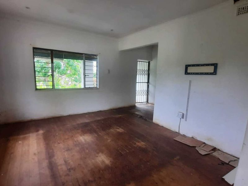 An empty living room featuring original timber flooring, metal window frames, and a security gate, requiring cosmetic updates to restore its appeal.