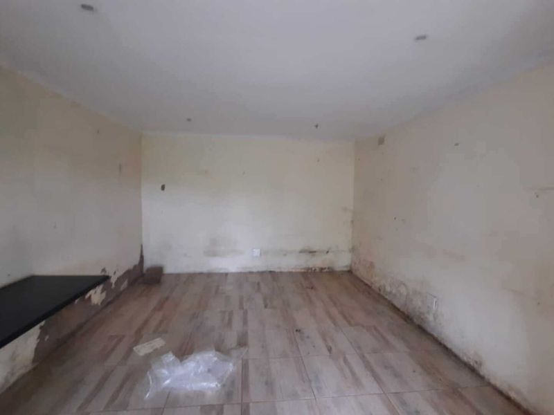 An empty living room space featuring tiled flooring and recessed lighting, currently requiring wall repairs and cosmetic refurbishment.