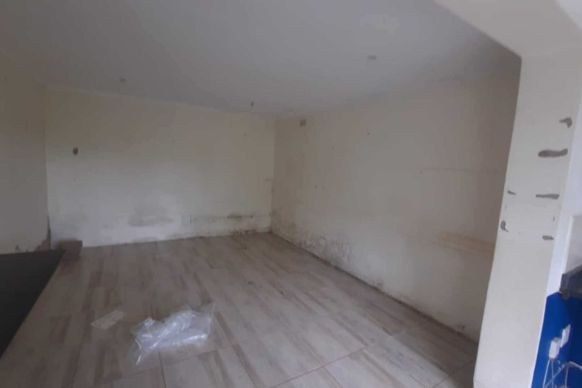 An empty living area featuring tiled flooring and recessed lighting, currently requiring wall repairs and cosmetic updates.