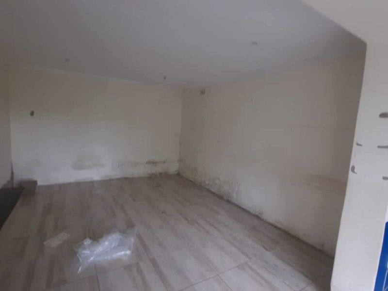 An empty living area featuring tiled flooring and recessed lighting, currently requiring wall repairs and cosmetic updates.