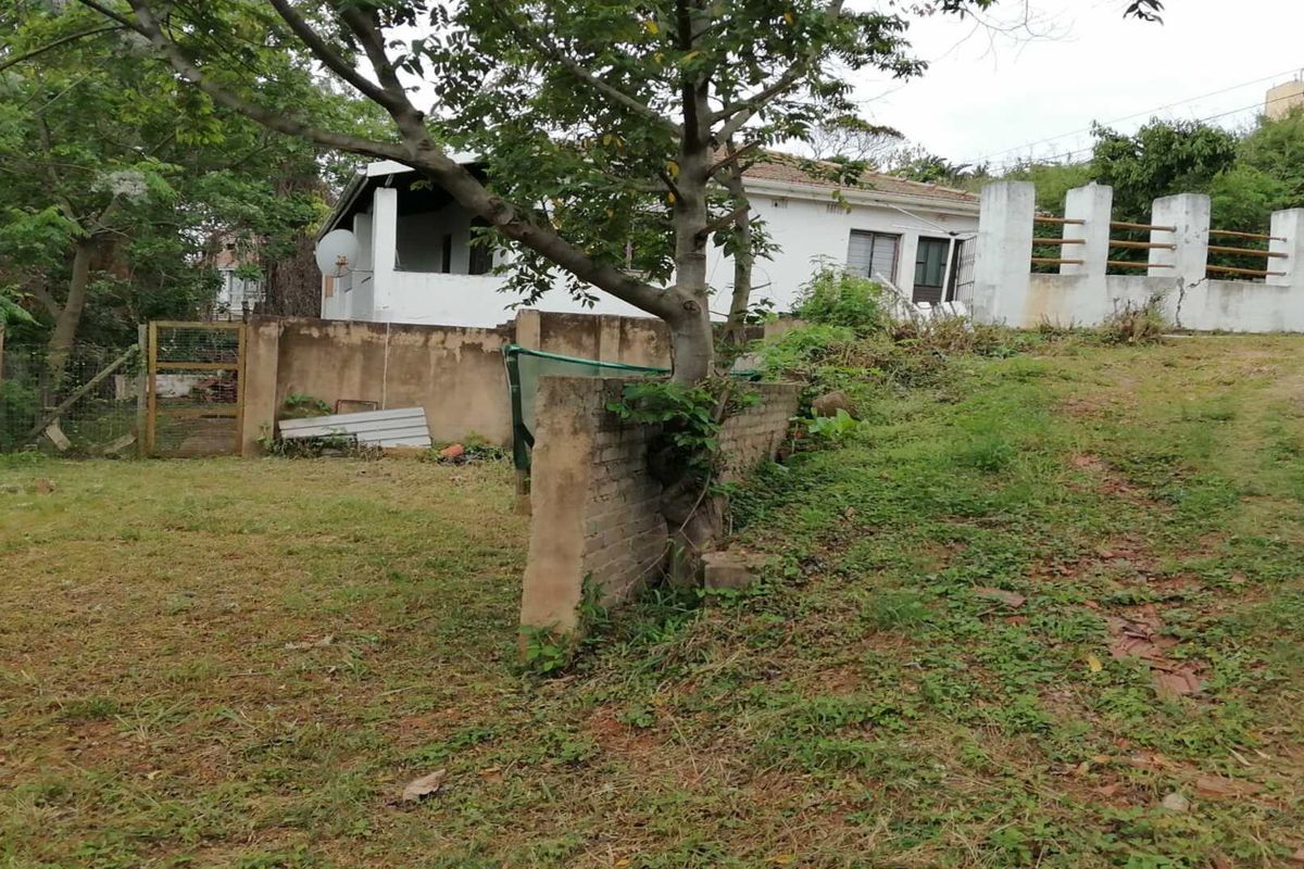 Rear view of the property showing a large garden area, brick boundary walls, and the rear elevation of the house with a tiled roof.