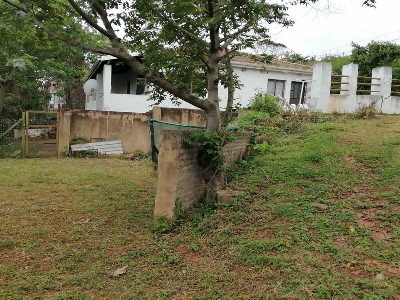 Rear view of the property showing a large garden area, brick boundary walls, and the rear elevation of the house with a tiled roof.