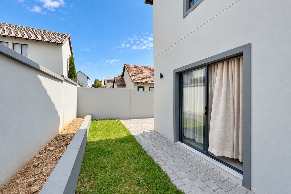 A neat rear garden area featuring a paved walkway, a small lawn, and a modern sliding door providing access to the home.