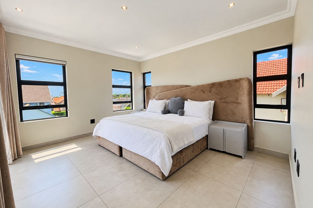 Spacious bedroom featuring neutral tiled flooring, modern aluminium-framed windows, and recessed downlighting, offering a bright and clean living environment.