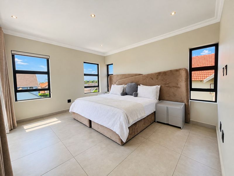 Spacious bedroom featuring neutral tiled flooring, modern aluminium-framed windows, and recessed downlighting, offering a bright and clean living environment.