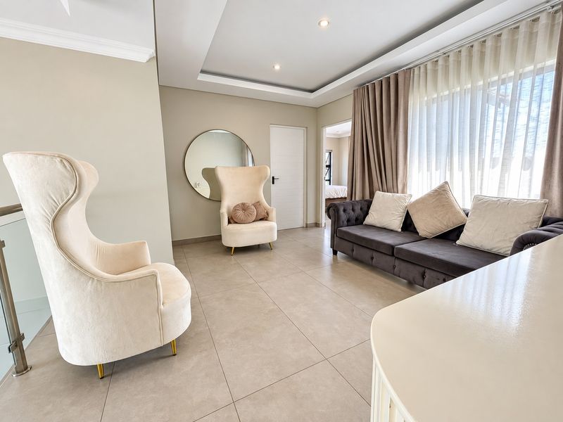 A bright and modern living room featuring neutral tiled flooring, a recessed ceiling with integrated lighting, and large windows with floor-to-ceiling curtains.
