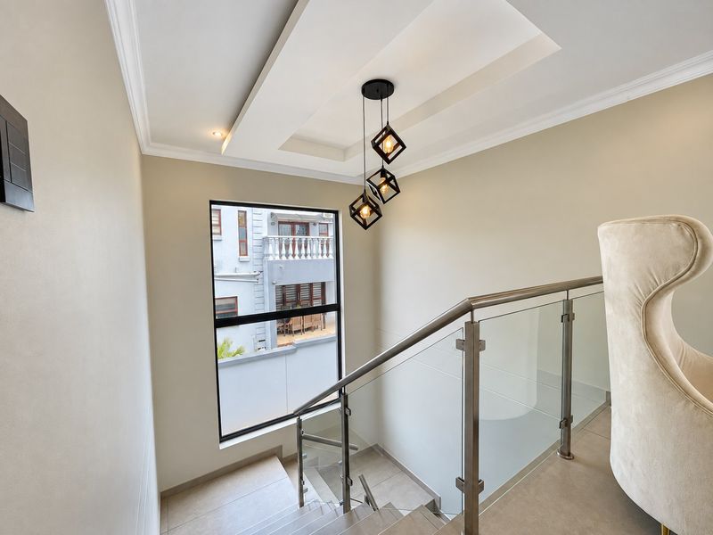 Modern staircase area featuring a sleek glass balustrade with stainless steel handrail, complemented by a stylish geometric pendant light and recessed ceiling detail.
